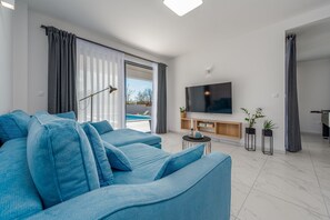 A modern living room with a large sofa, a flat-screen TV, and a view of a pool. - Villa Merci Zadarvillas (Privlaka)