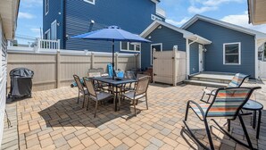 A patio with a table and chairs, a blue umbrella, and a brick floor. - Coffee | BBQ Grill | Outdoor Dining | Wifi (Belmar)