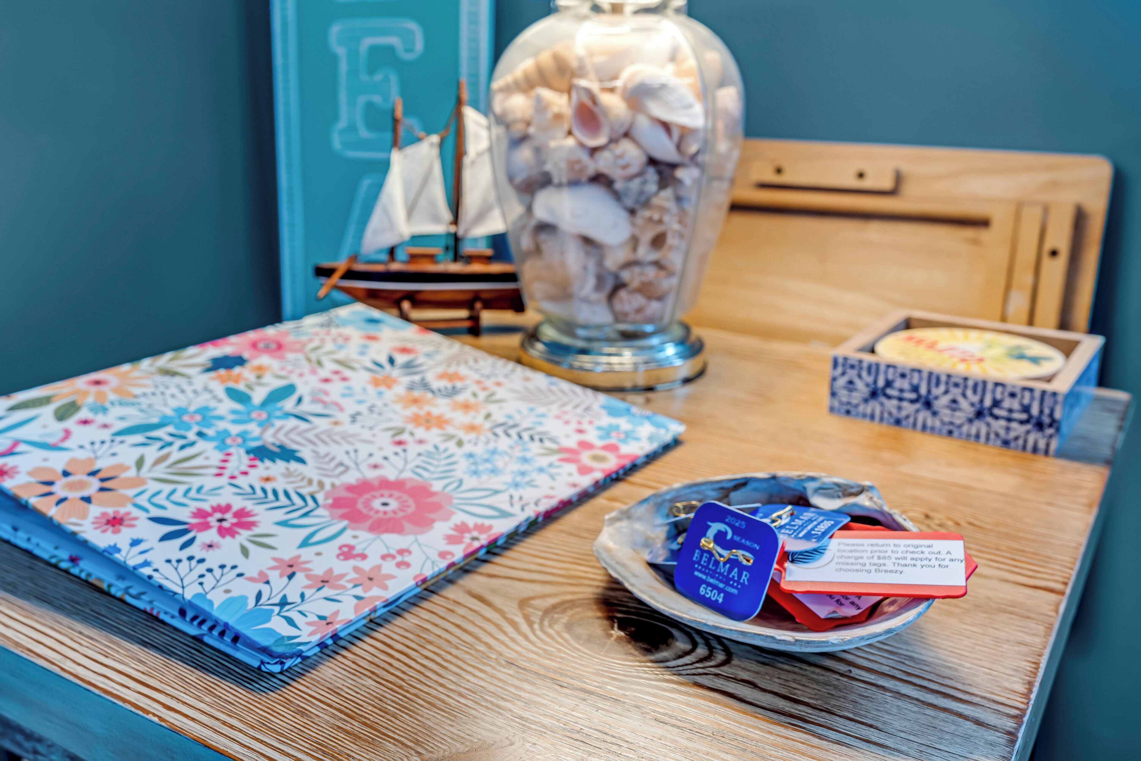 A wooden table with a floral notebook, a decorative jar of seashells, and a small box with a card.