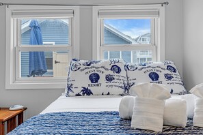 Et soveværelse med to vinduer, en seng med et blåt og hvidt mønstret sengetæppe, to puder med teksten 'Ocean View Resort' og et natbord med en telefon.