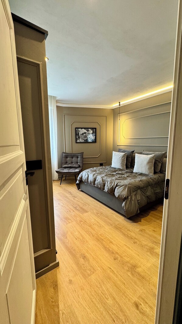 A bedroom with a bed, a chair, a painting on the wall, and a door.