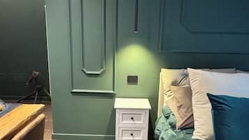 Ein Schlafzimmer mit grüner Wand, einem Bett mit vielen Kissen, einem Nachttisch und einem Sessel.