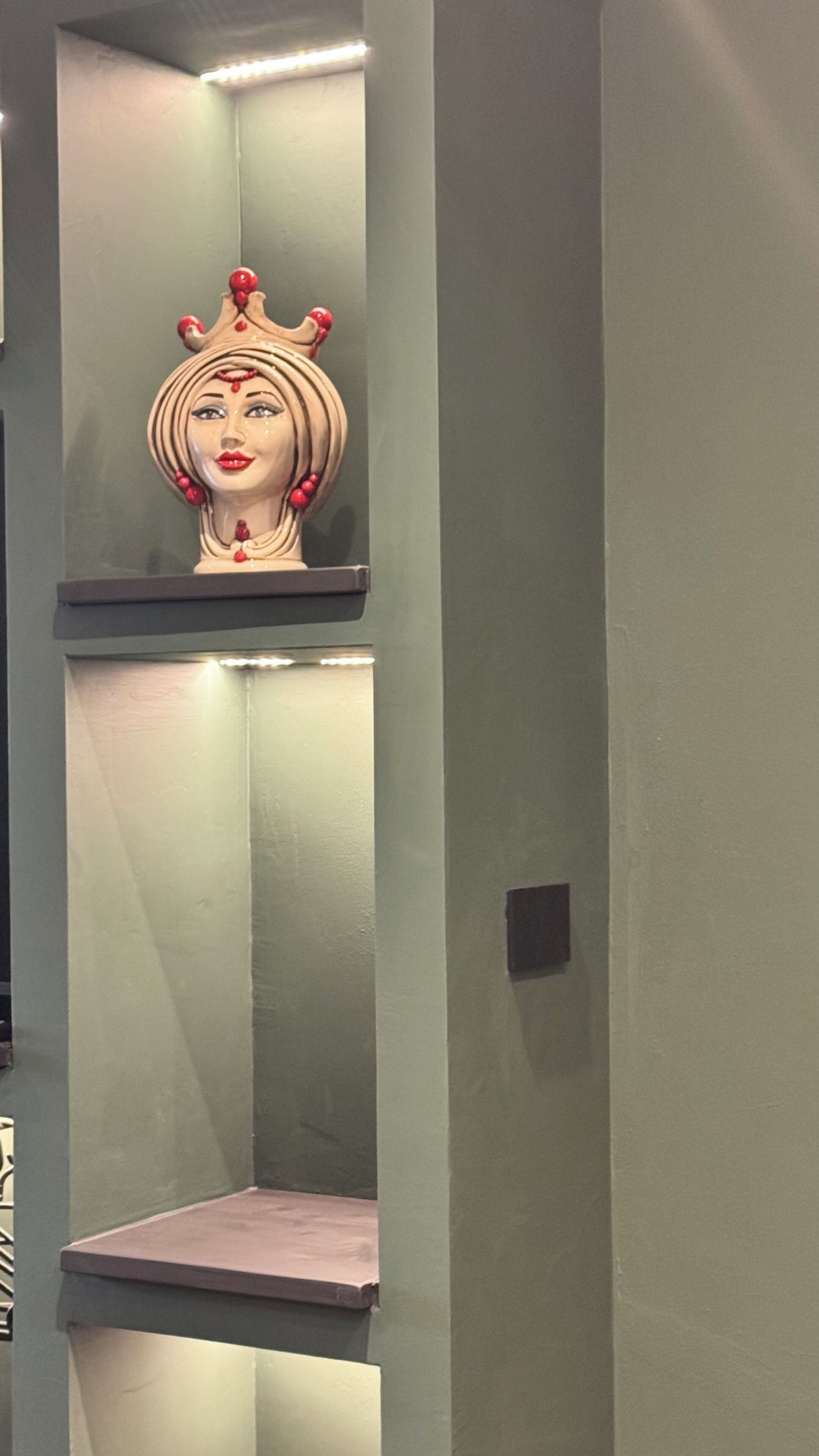 Eine Wand mit einer dekorativen Büstenstatue und einem Regal.