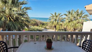 A balcony with a table and chairs, overlooking a beach with palm trees and the sea. - Beautiful apartment Lilou in 1st line sea view, swimming pool and palm trees (Piles)
