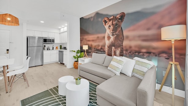 A modern living room with a grey sofa, white chairs, and a large painting of a lion. - Lake Buena Vista Vacation Rental (Orlando)