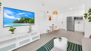 A modern living room with a flat-screen TV, white cabinetry, a dining area, and a kitchen with stainless steel appliances. - Lake Buena Vista Vacation Rental (Orlando)