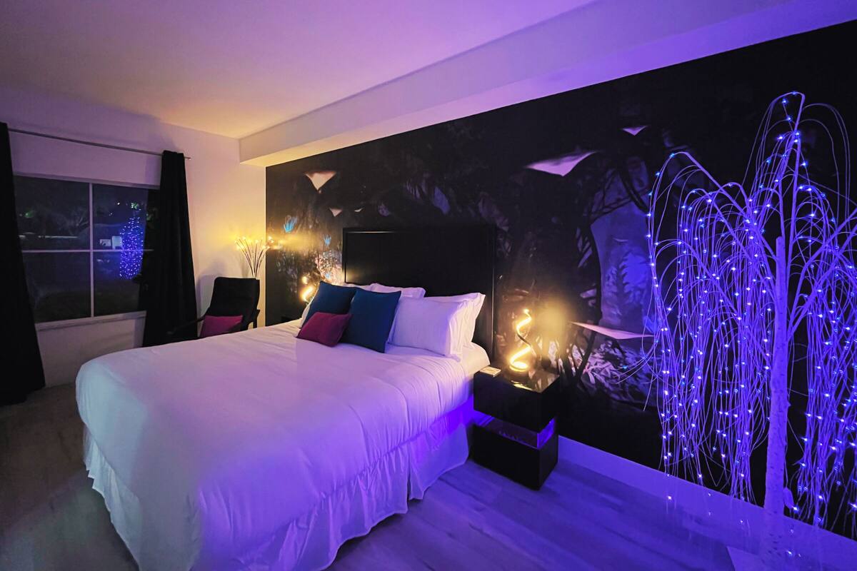 A modern bedroom with a large bed, a wall-mounted TV, and ambient lighting.