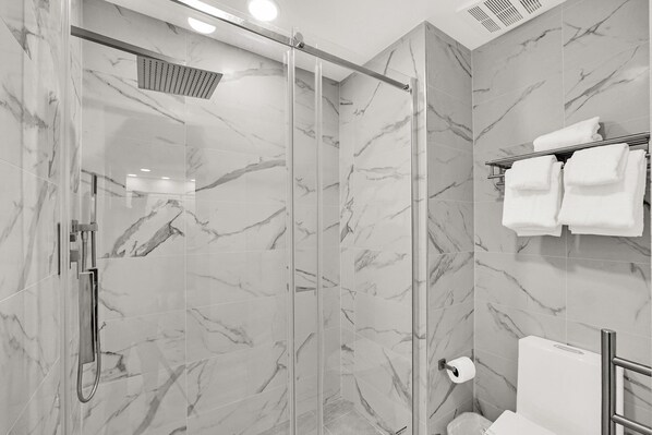 A modern bathroom with a glass-enclosed shower, marble walls, and a towel rack with folded towels. - Lake Buena Vista Vacation Rental (Orlando)