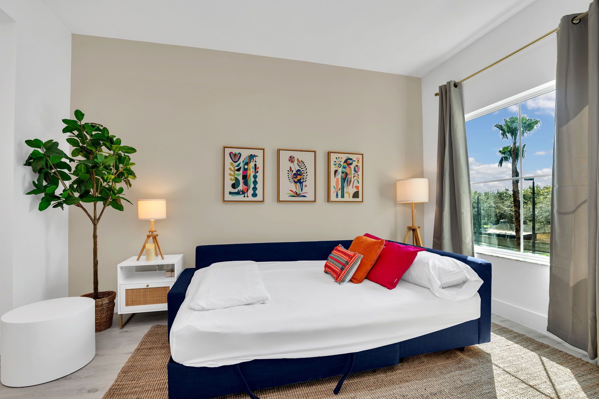 Une chambre d’hôtel moderne avec un grand lit, deux lampes de chevet, une plante en pot et trois œuvres d’art encadrées accrochées au mur.