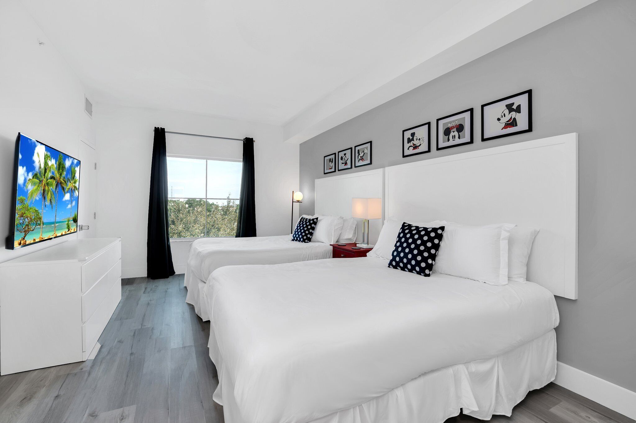 A hotel room with two beds, a TV, a desk, and a window with curtains.