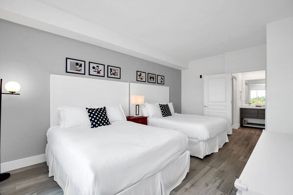Habitación de hotel con dos camas, una mesita de noche con lámpara, cómoda y cuadros en la pared.