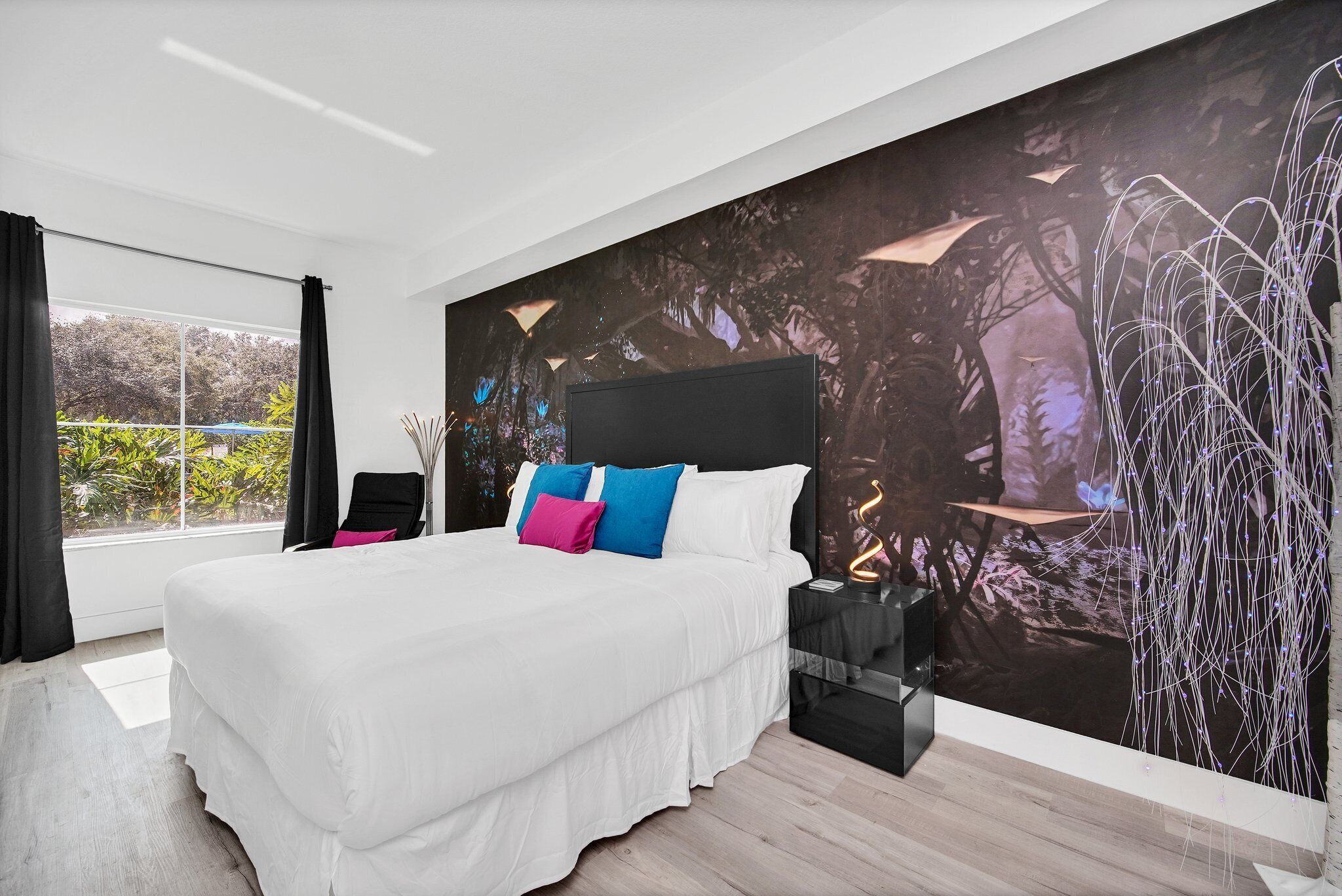 A modern bedroom with a large bed, a nightstand, and a wall mural.