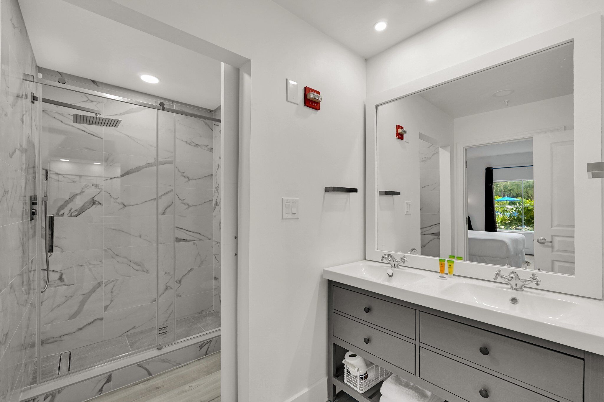 Un baño moderno con ducha envuelta en vidrio, un espejo grande y un tocador blanco con cajones.
