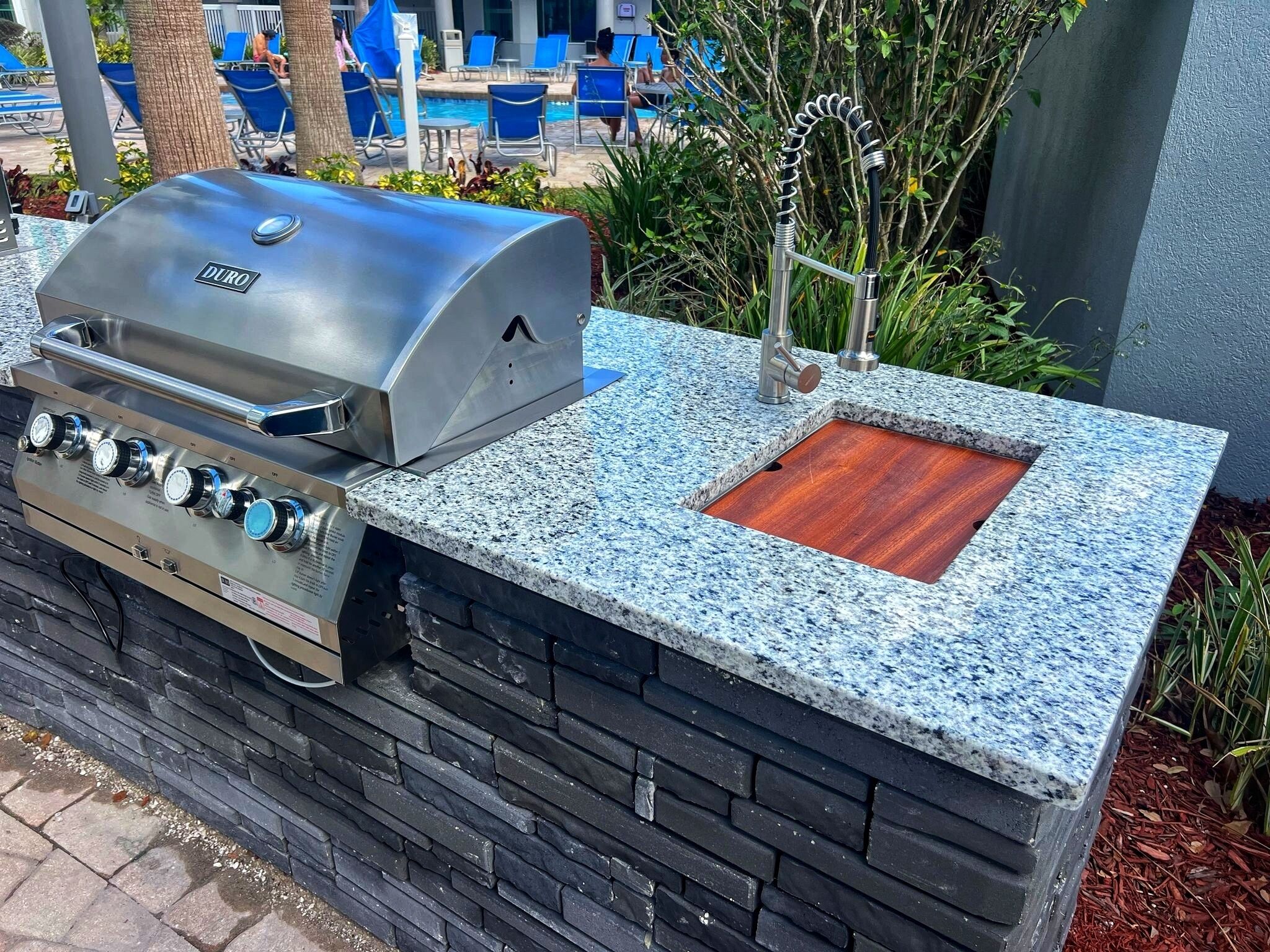 Eine Außenküche mit integriertem Grill, Spüle und Arbeitsplatte aus Stein.