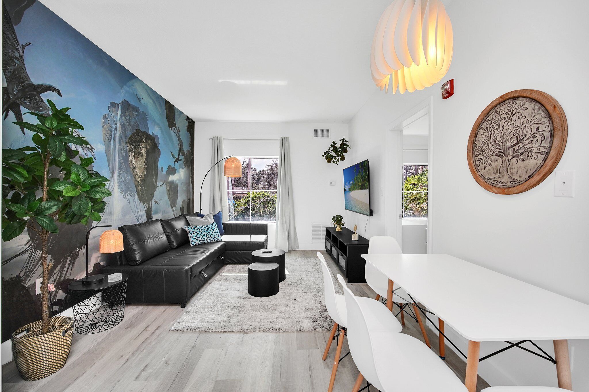 A modern living room with a black sofa, white dining table, and a large abstract painting on the wall.