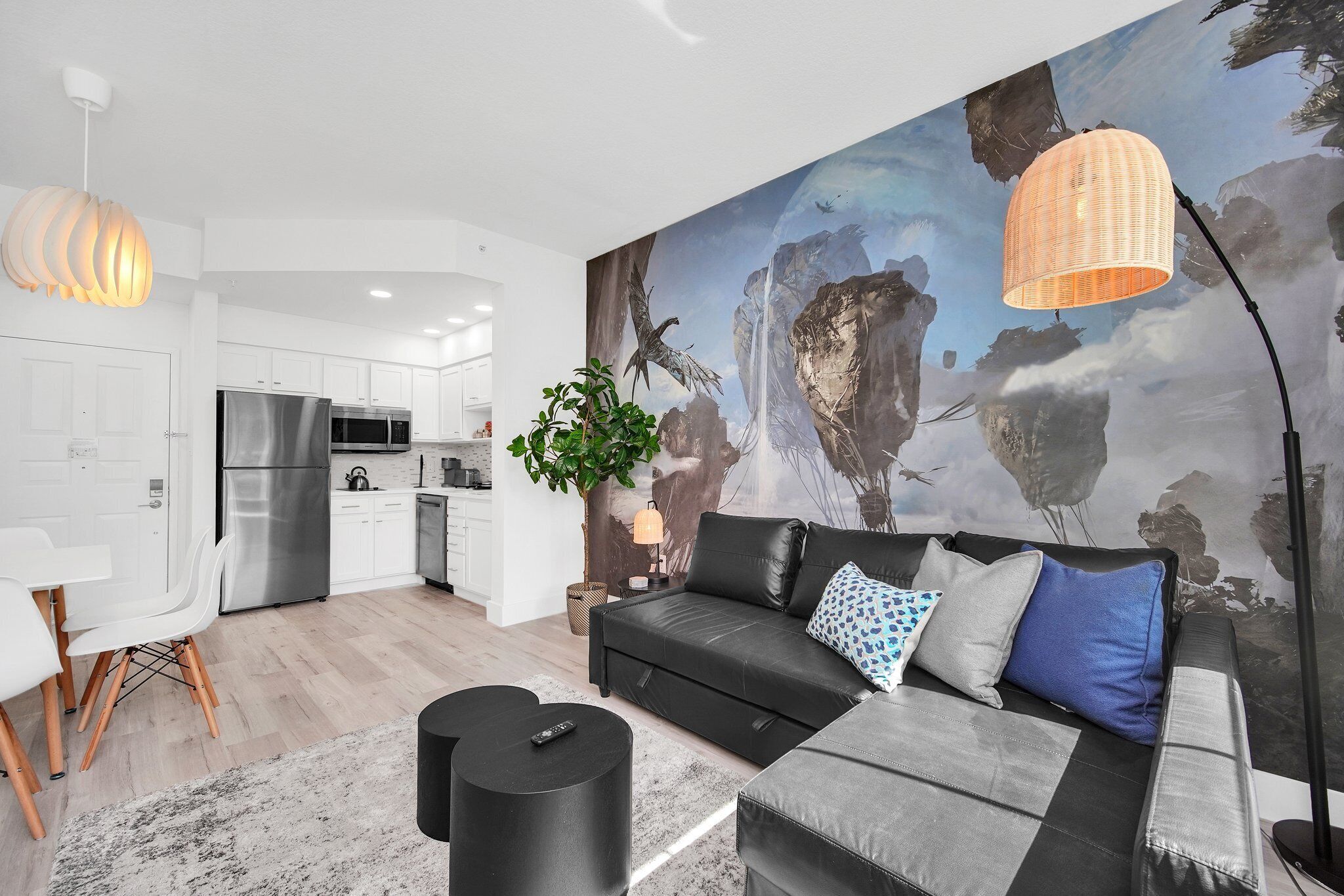 Ein modernes Wohnzimmer mit einer schwarzen Ledersofa, einem Essbereich mit weißen Stühlen und einer Küche mit Edelstahlgeräten.