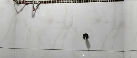 Un baño con inodoro blanco, cabezal de ducha e calentador de agua instalado en la pared.