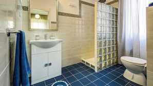 A bathroom with a white sink, mirror, and toilet, tiled floor, and a shower area with a glass door. - Family run bed and breakfast. (Alghero)