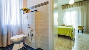 A bathroom with a toilet, shower, and a bed with a yellow bedspread. - Family run bed and breakfast. (Alghero)