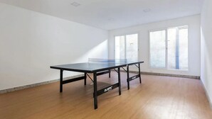 Una habitación con mesa de ping pong, ventanas amplias y suelo de madera.