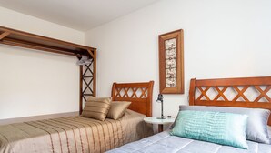 Un dormitorio con cama, mesita de noche, lámpara y un cuadro colgado en la pared.