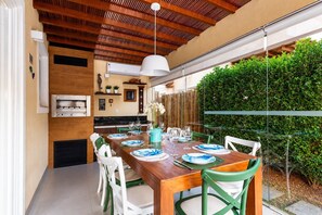 An outdoor dining area with a wooden table, green and white chairs, and a hanging light fixture.