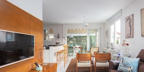 Uma sala de estar moderna com uma televisão grande, móveis de madeira e uma área de jantar com cadeiras e uma mesa.