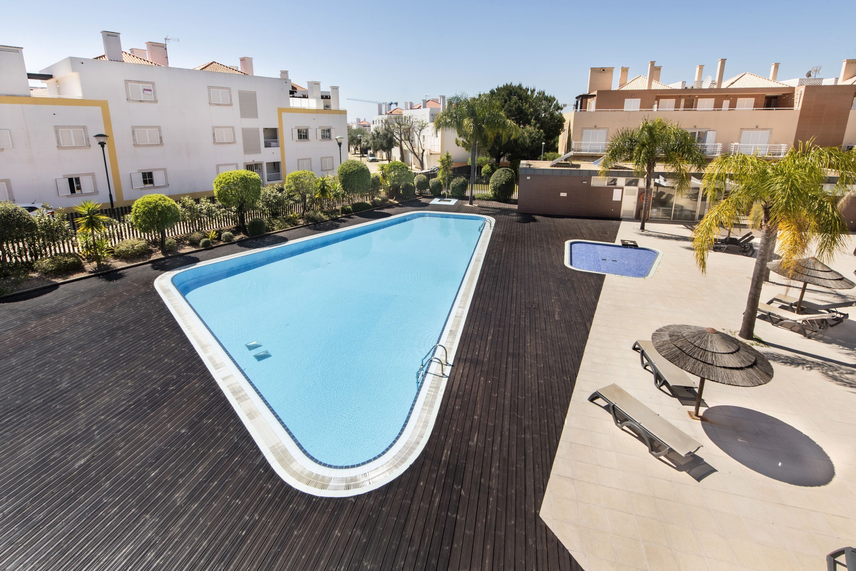 Piscina en la azotea con terraza de madera, rodeada de vegetación y edificios residenciales.