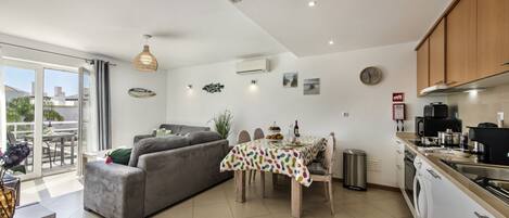A modern kitchen with a dining area, a grey sofa, and a dining table with a colorful tablecloth.