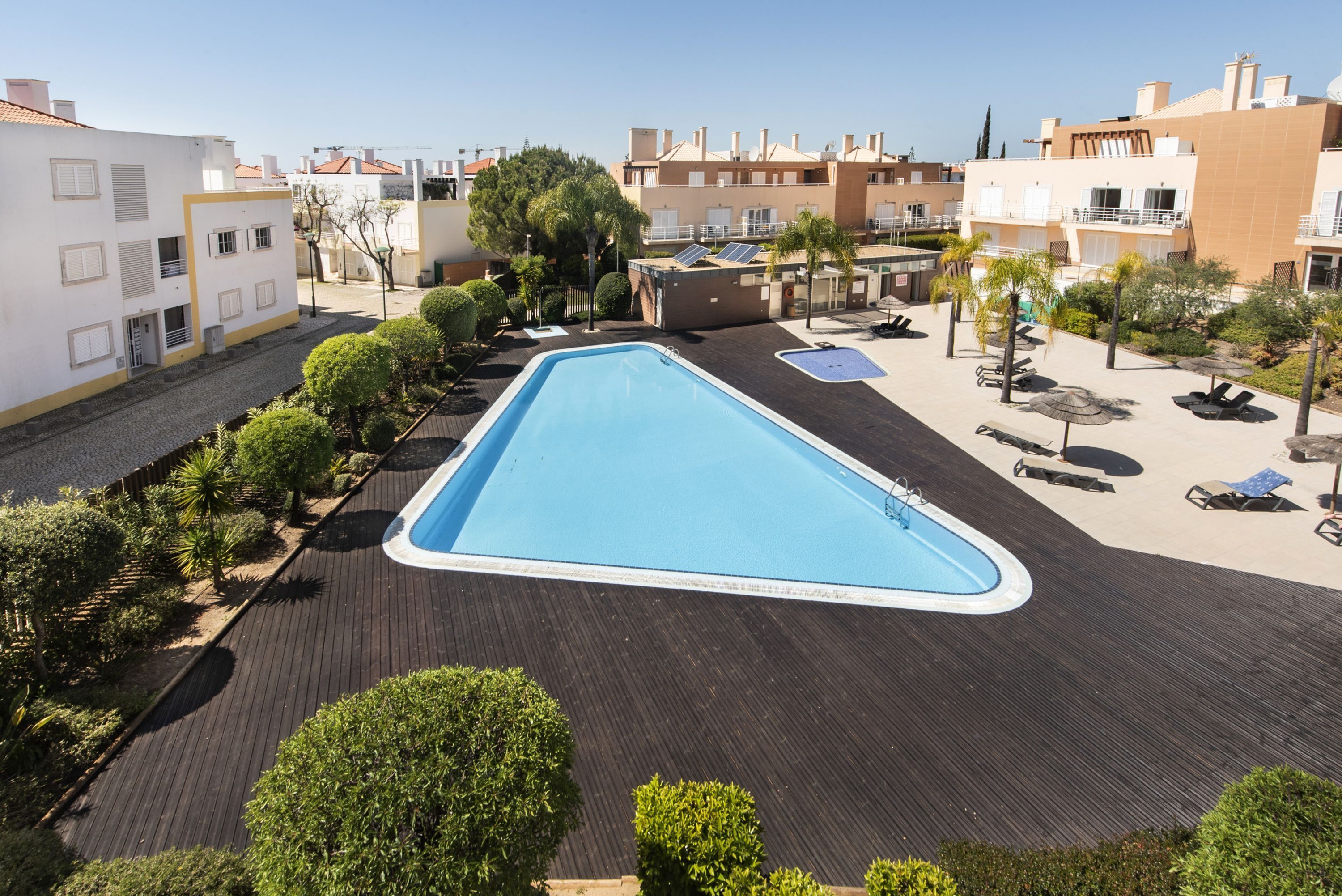 A swimming pool surrounded by a wooden deck, with buildings in the background.