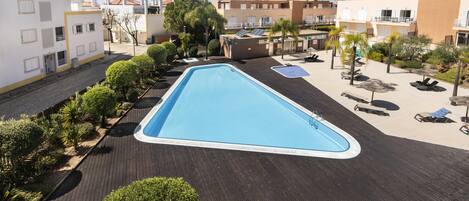 A swimming pool surrounded by a wooden deck, with buildings in the background.