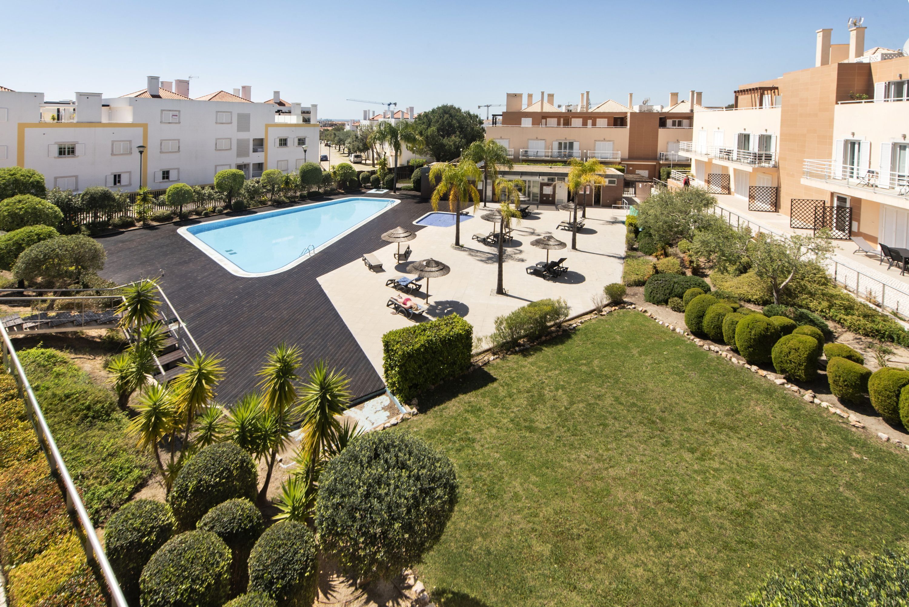 A rooftop pool area with a swimming pool, sun loungers, and a well-maintained lawn.