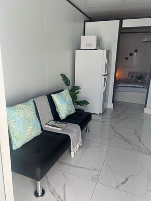 Ein stilvolles Wohnzimmer mit einer schwarzen Couch, einem weißen Kühlschrank und einem Bett mit gemustertem Überwurf.