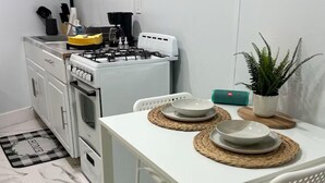 A compact kitchen with white cabinets, a gas stove, and a dining table set with plates and a potted plant.