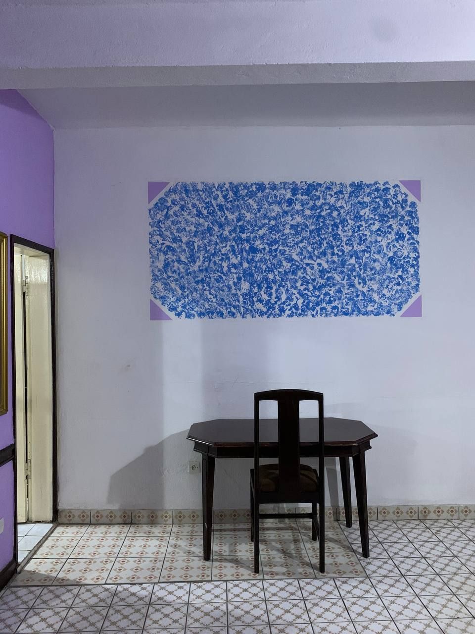 A room with a tiled floor, a table with a chair, and a wall with a blue floral pattern.