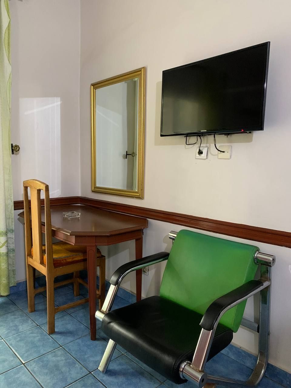 Una habitación con una mesa de comedor de madera, una silla verde y negra, un televisor montado en la pared y un espejo.