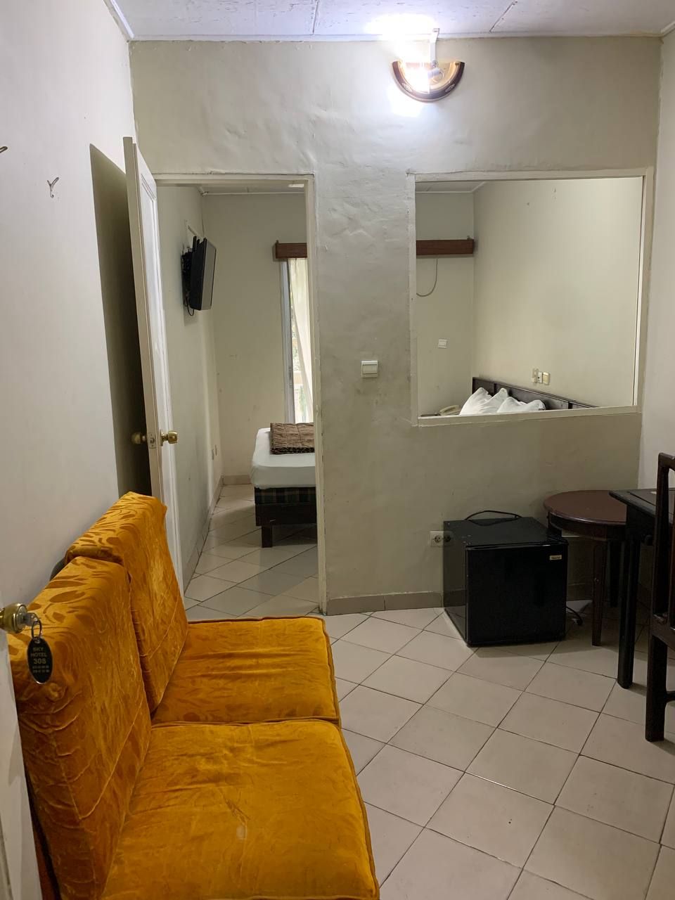 A compact room with a yellow sofa, a small table, a chair, a bed, and a mirror.