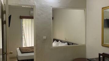 Une petite pièce comprenant un lit, une petite table, une chaise, un miroir et une fenêtre avec des rideaux.