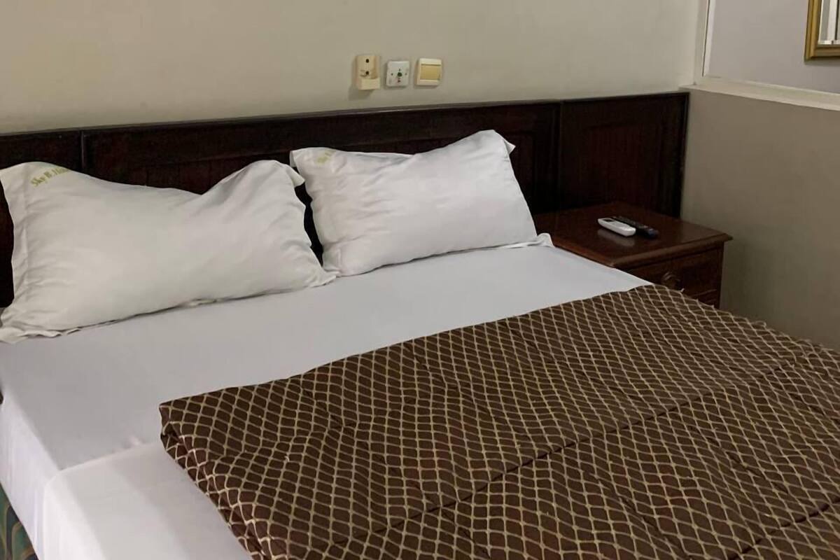A hotel room with a bed, a nightstand, and a wall-mounted light switch.