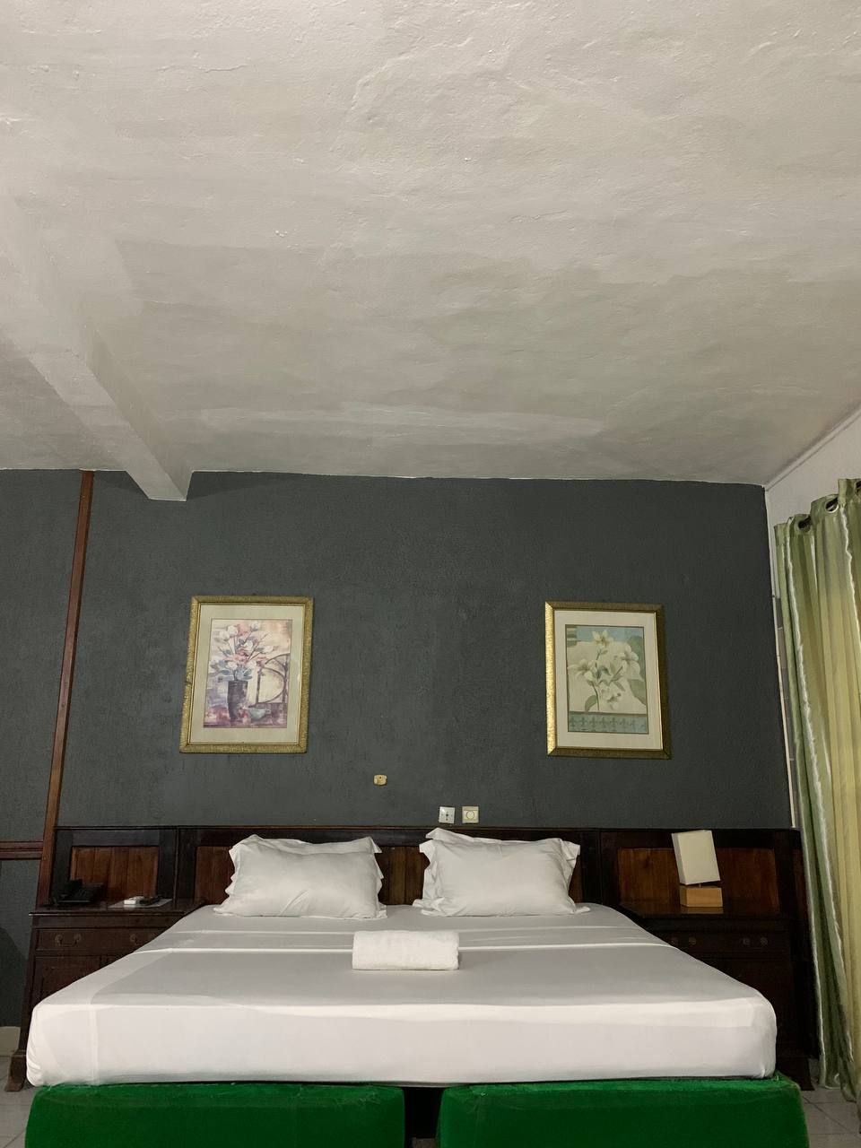 Habitación de hotel con una cama grande, dos cuadros enmarcados con motivos florales en la pared y un cabecero de madera.