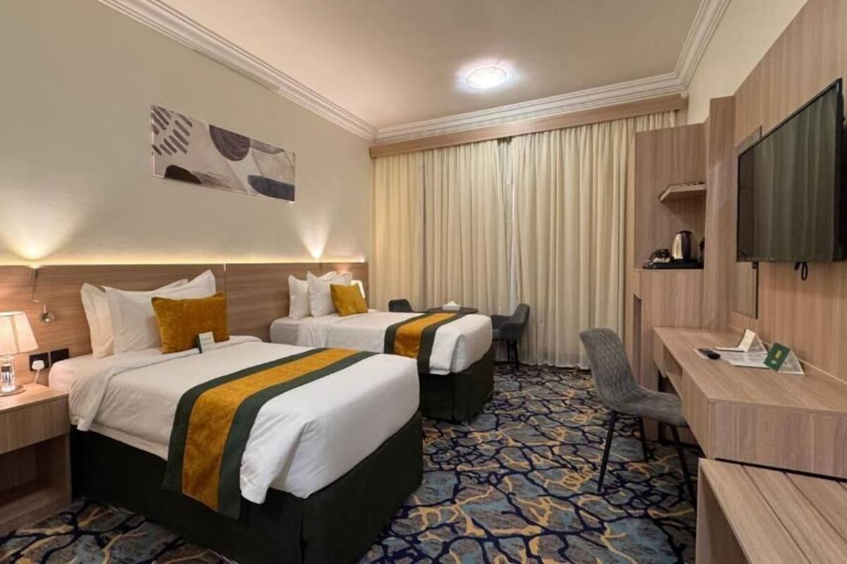 Une chambre d’hôtel avec deux lits, un bureau, une chaise, une télévision et une moquette à motifs.