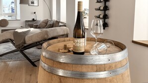 A modern living room with a wooden barrel, a wine bottle, and glasses on a table. There is a sofa and a lamp in the background. - WeinZeit13 (Neustadt an der Weinstraße)
