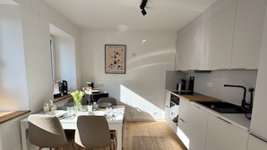 A modern kitchen with white cabinets, a wooden dining table with chairs, a kitchen island, and a hanging light fixture. - WeinZeit13 (Neustadt an der Weinstraße)