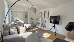 A modern living room with a sofa, armchair, and a TV on a stand. - WeinZeit13 (Neustadt an der Weinstraße)
