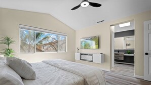 A bedroom with a bed, a ceiling fan, a window with a view, a mounted TV, and a bathroom visible through an open door. - “NEW” Half Moon Retreat / +Pool Table / - 5 min away from GRATON casino (Santa Rosa)
