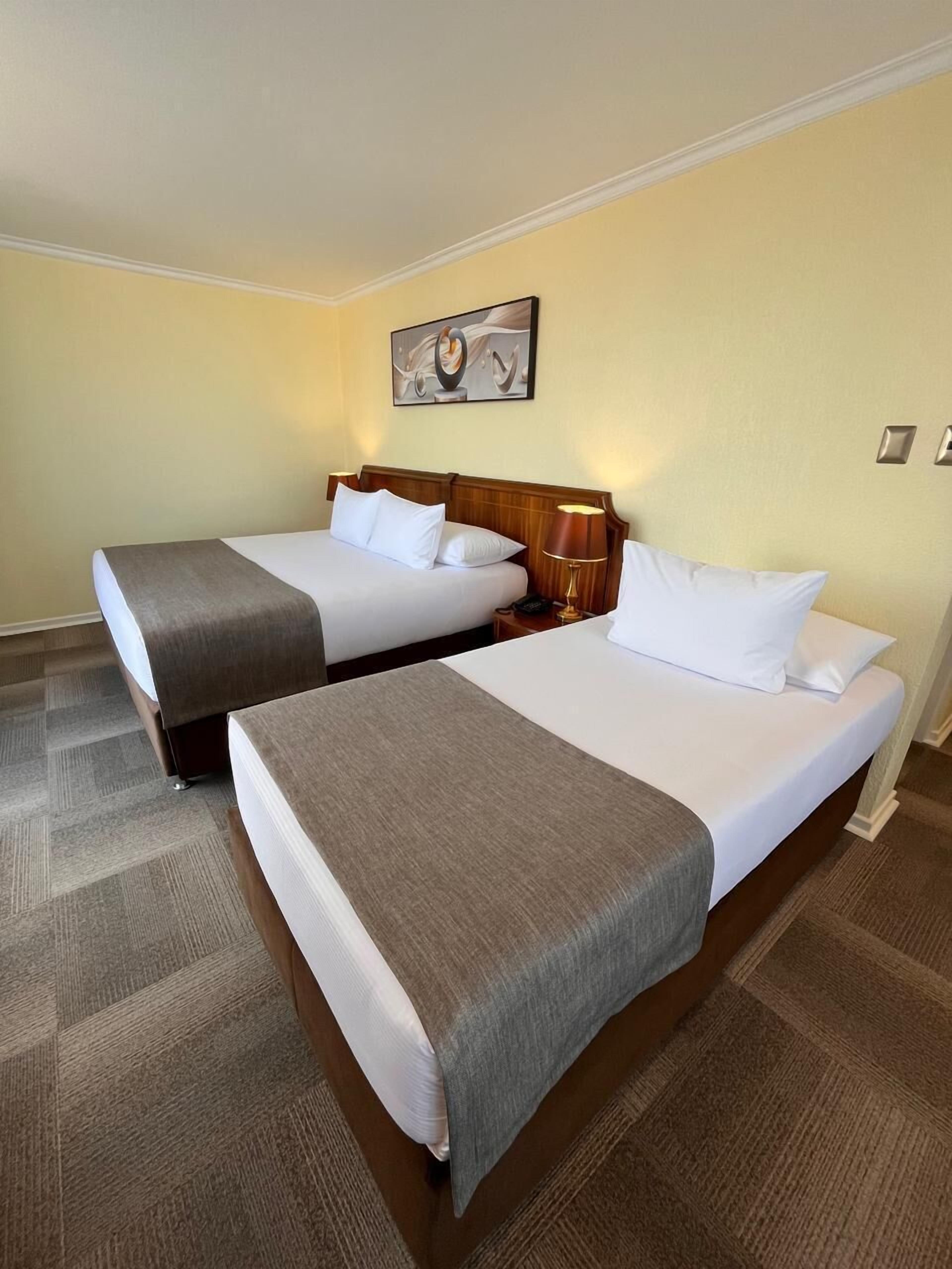 Two single beds with wooden headboards, white linens, and brown throw blankets. There is a nightstand with a lamp between the beds.