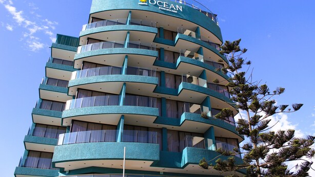 Un hôtel à plusieurs étages doté de balcons, une enseigne indiquant « OCEAN BOULEVARD », et un ciel bleu clair en arrière-plan.