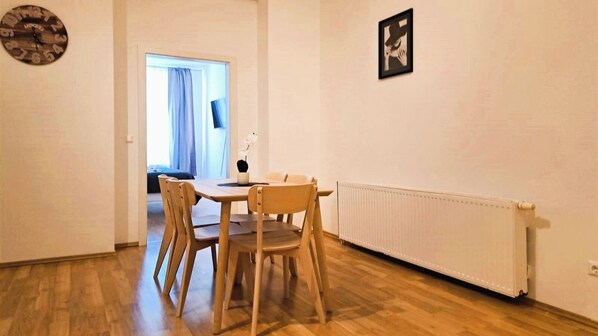 A dining area with a wooden table and chairs, a clock on the wall, and a radiator.