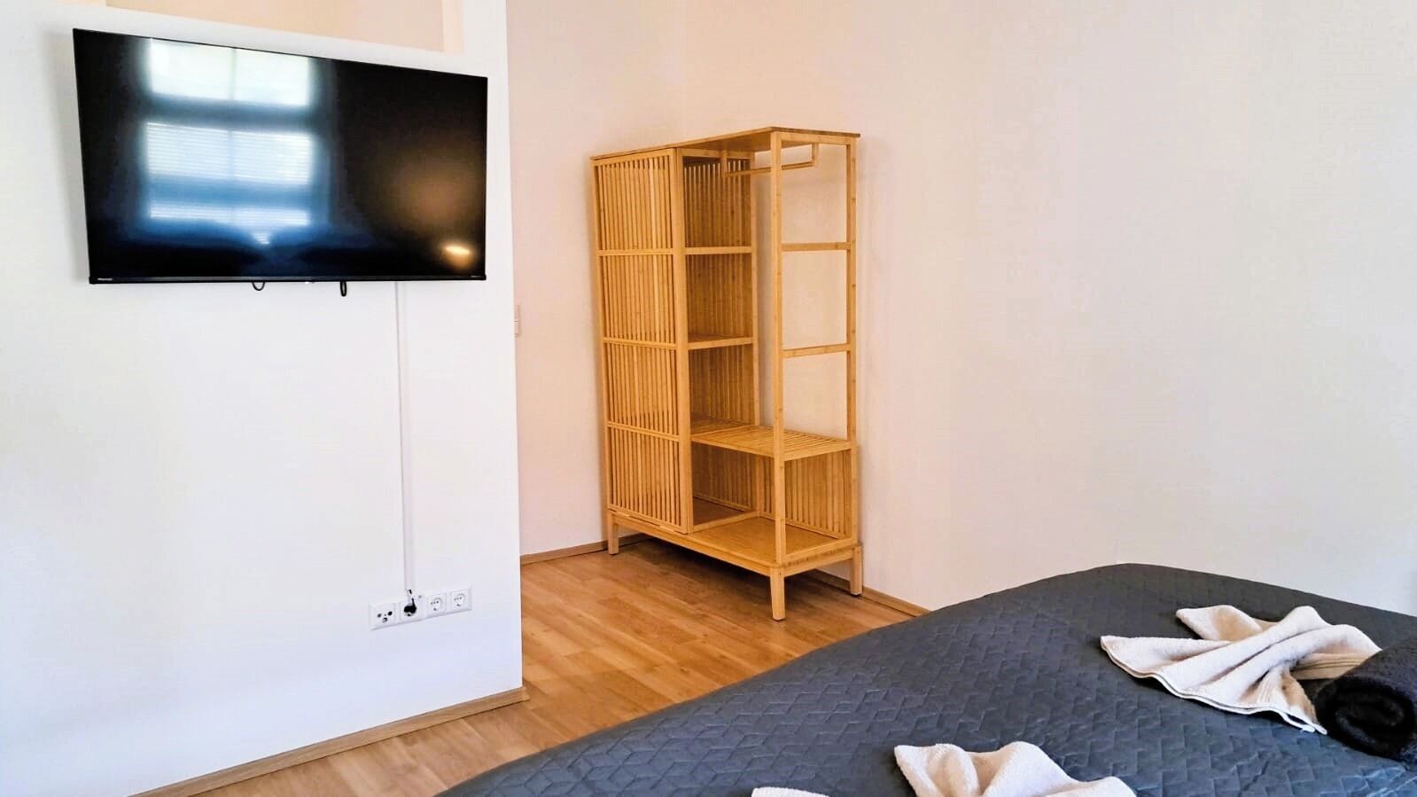 A room with a bed, a TV mounted on the wall, and a wooden shelving unit.