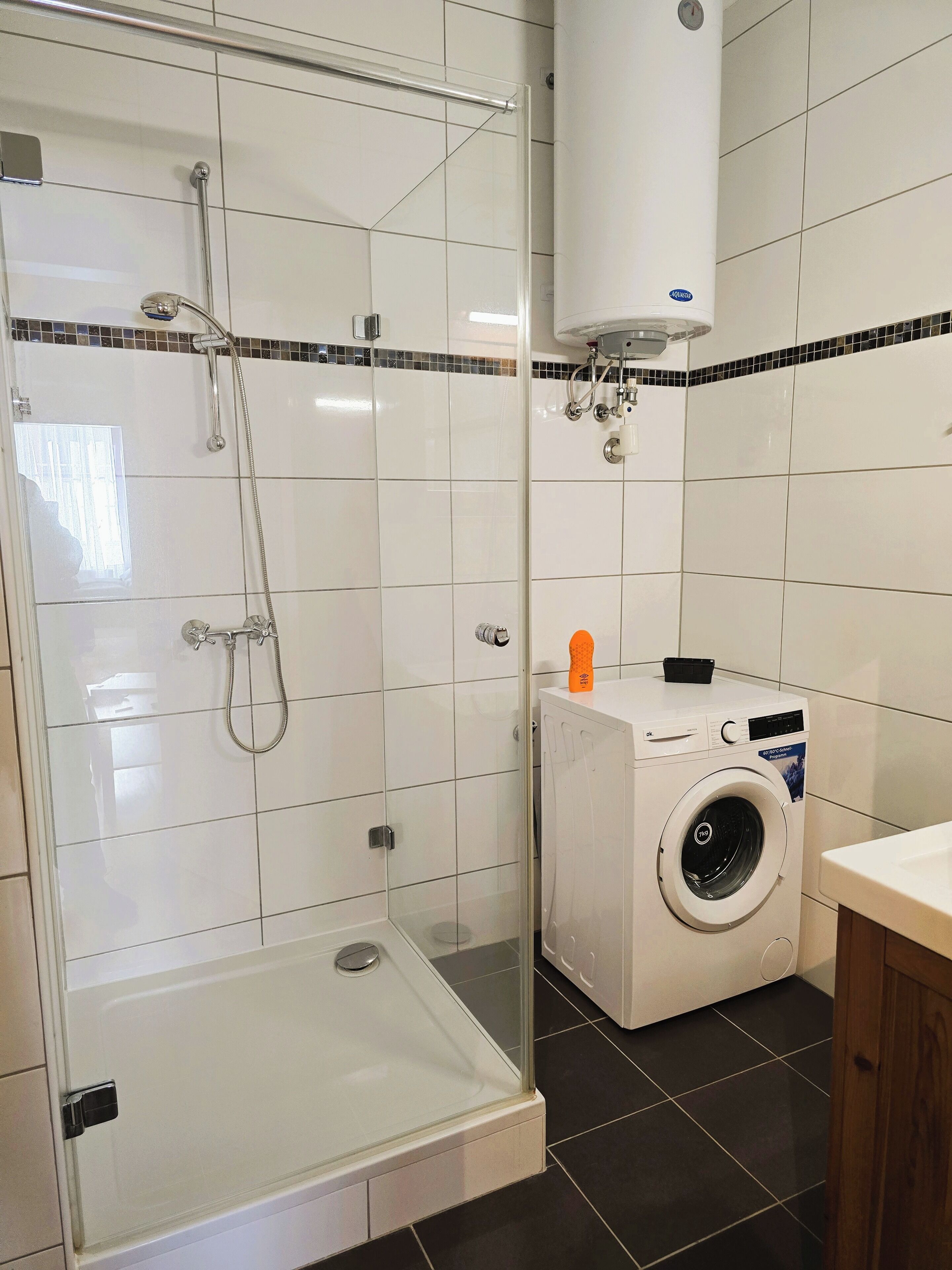 A bathroom with a glass-enclosed shower, a washing machine, and a toilet.